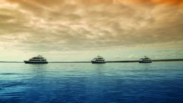 Three of the best Galapagos cruise small yachts lined up side by side with blue water and an orange sky.