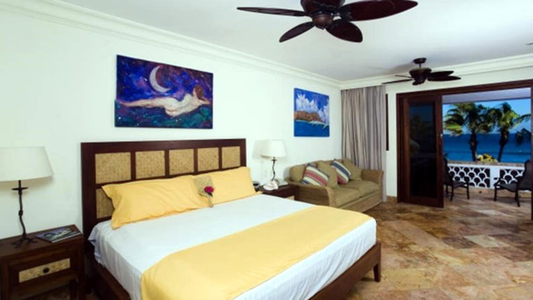 A queen-sized bed in a room with a ceiling fan, art, and marble floors at the Cabo Surf Hotel in Baja California