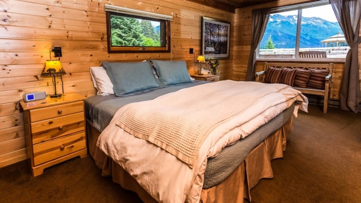 Inside the Stellar's Jay Cabin with a wood interior, cozy decor, queen-sized bed, and a large window, at the Tutka Bay Wilderness Lodge in Alaska