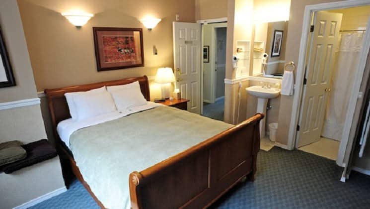 Carpeted guest room with queen bed and small sink at Copper Whale Inn in Anchorage, Alaska