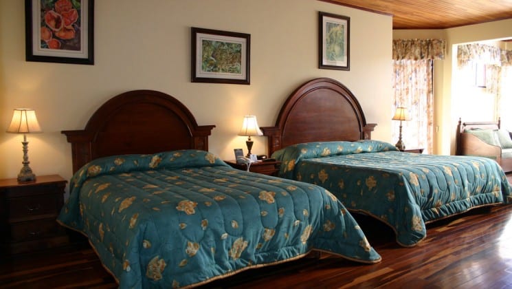 Room interior with wooden floors, two beds with wooden headboards, bedside tables and couch at Hotel Fonda Vela in Monteverde, Costa Rica