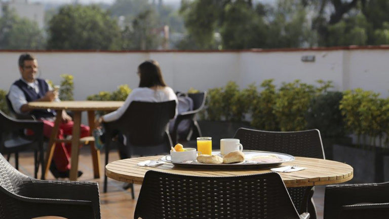 Breakfast with orange juice, fruit, and fresh bread is served on a table in an outdoor courtyard, where people are enjoying the morning buffet at the Casa Andina Standard Arequipa in Peru.