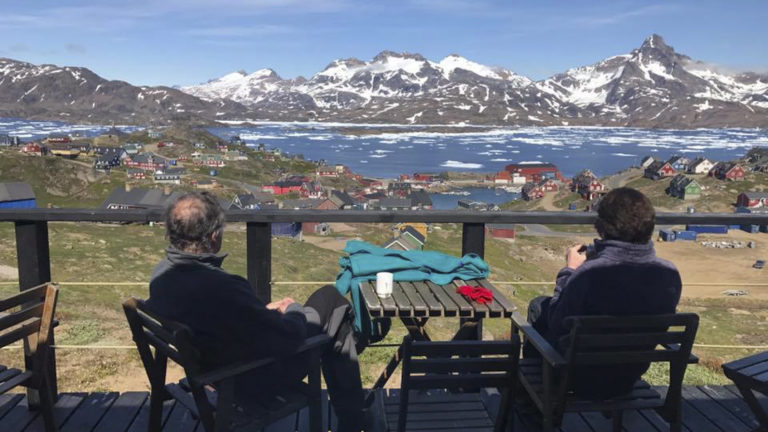 Two guests at the Hotel Kulusuk sit on the patio and take in views of Greenland's arctic waters and rocky mountain bluffs