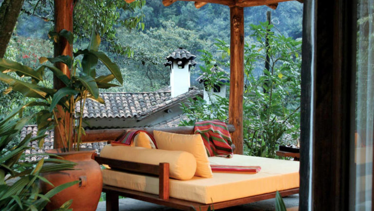 A terrace with a sitting area and loveseat overlooks a lush garden at the Inkaterra Machu Picchu Pueblo Hotel, a National Geographic Unique Lodge of the World.