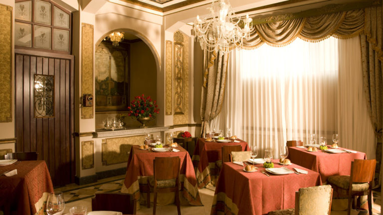 The ornately decorated dining room, with red tablecloths, fine silverware and settings, curtains and drapes, and a chandelier at Mansion del Rio, a premier boutique hotel in Guayaquil, Ecuador