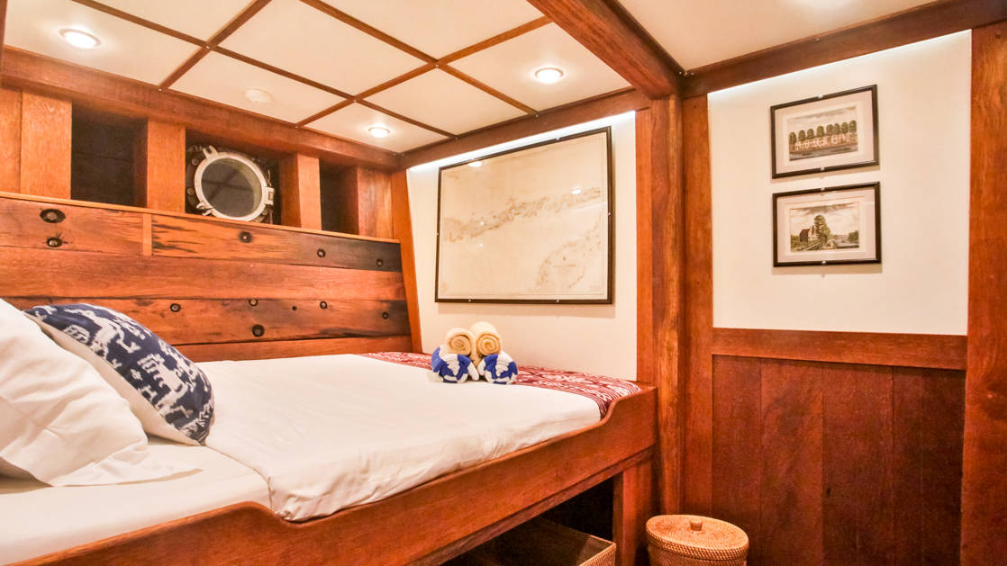 a cabin on the ombak putih small ship showing the higher of 2 beds, wooden walls and pictures on the walls