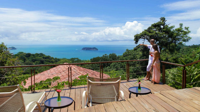 A deck with lounge chairs and small tables overlooks the red tiled roofs at Si Como No, a boutique resort, and the Pacific Coastline in Costa Rica