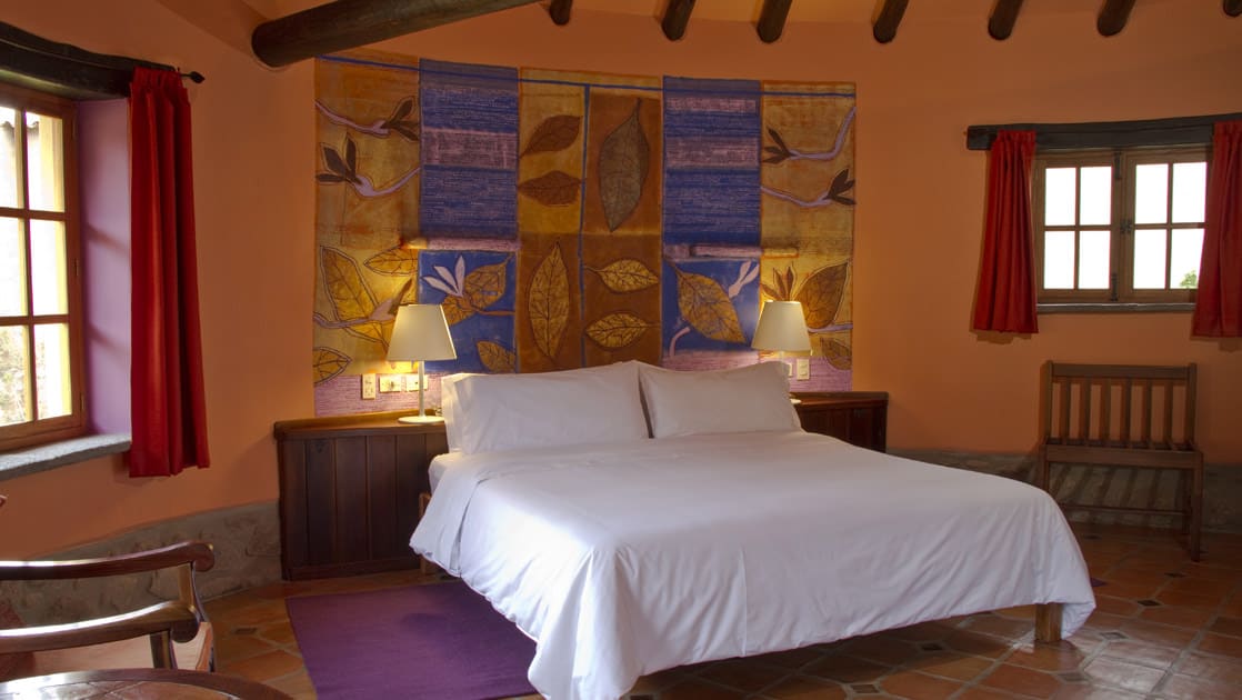 The superior casita room with a king bed, decorative tiled walls, windows, and reading lights at Sol y Luna, a sustainable, luxury retreat in Urubamba, one hour’s drive from Cusco.