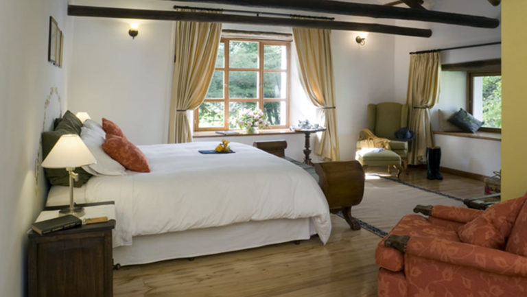 Room interior with bed, bedside tables, bench, armchair, window seat at Hacienda Zuleta in Ecuador