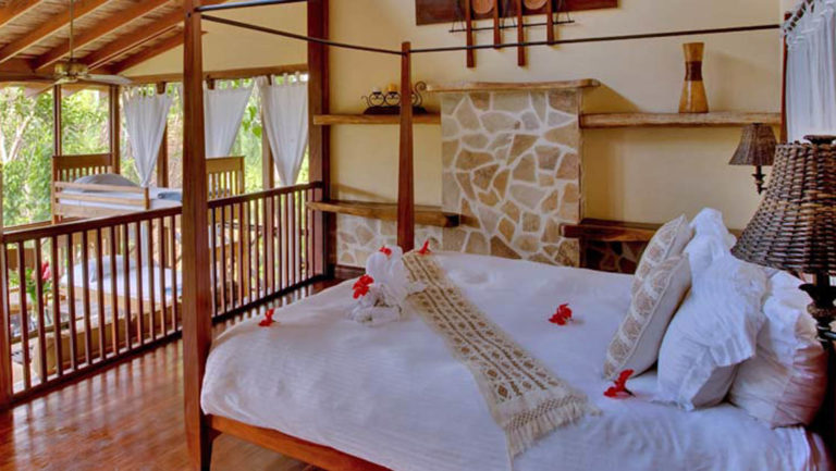 Master bedroom loft with large bed and twin bunk beds surrounded by lush forest at Caves Branch Jungle Lodge in Belize