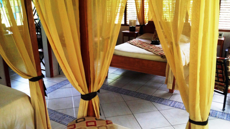 Four-post bed with yellow curtains and tile floor in a deluxe bungalow at Casa Corcovado Jungle Lodge in Costa Rica