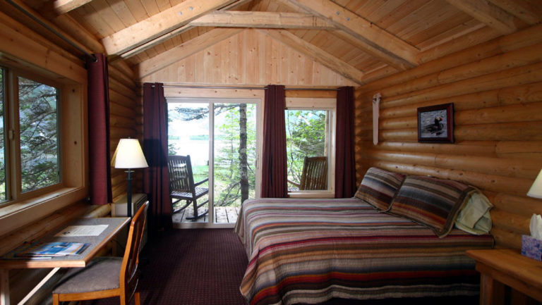 Inside one of the private guest log cabins at the sustainable Kenai Fjords Glacier Lodge in Alaska, with a queen sized bed and a view of the forest