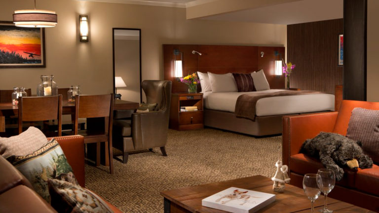 The suite at the Lakefront Anchorage with a king bed, chairs and tables, and seating. This luxury hotel is a stopover for those exploring the Alaskan wilderness