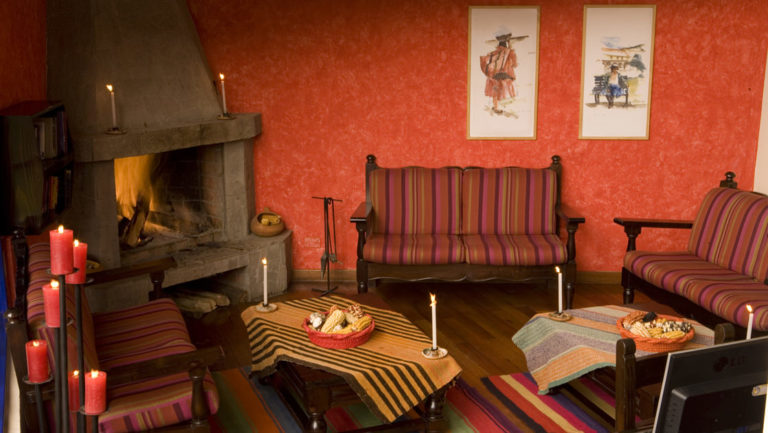 The lobby at Casa Andina Classic Cusco San Blas, in Cusco, Peru, is warm and inviting with a wood-fired stove, wooden benches, painted walls, artwork, and woven textiles.