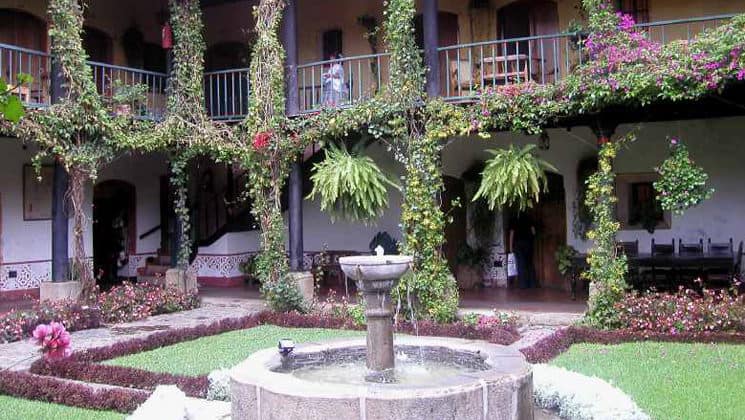 A courtyard with green grass, garden beds, and a fountain inside the Posada Don Rodrigo, a renovated colonial-era hotel in Antigua
