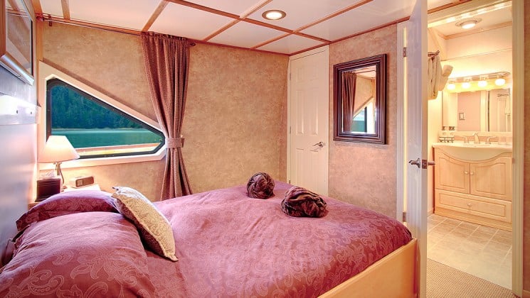 commander cabin with a large red bed and triangle window looking outside aboard the Safari Quest san juan islands small ship