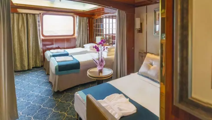 Two small beds, one large bed and large window of Triple Suite aboard Sea Spirit small ship