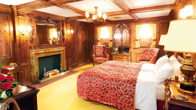 Lindblad Sea Cloud mediterranean luxury small ship cabin with a large bed, fireplace, comfortable chairs, wood walls and a chandelier