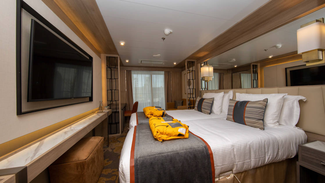 Veranda Suite with double bed, two yellow parkas and sitting area aboard World Explorer small polar ship.