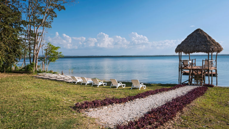 Several lounge chairs on the beach of a lake Camino Real Tikal Hotel in Guatemala