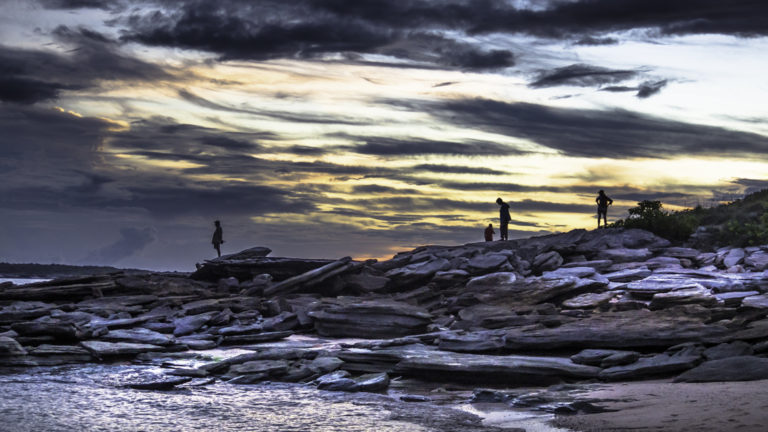 travelers explore a rocky shoreline at sunset on the Cape York and Arnhem Land small ship cruise