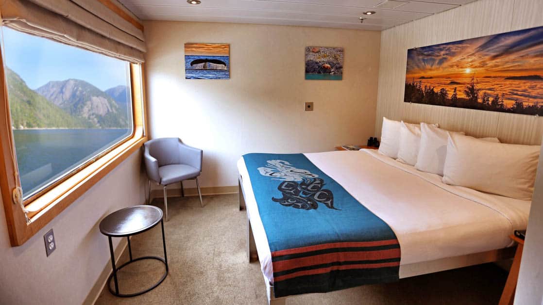Deluxe stateroom aboard Chichagof Dream with large window, bed, and paintings.