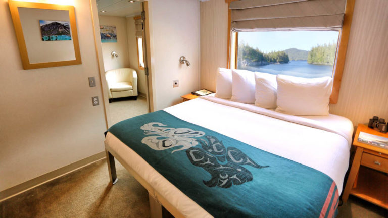 Main Deck Deluxe Suite aboard Chichagof Dream with large bed, window, and chair.