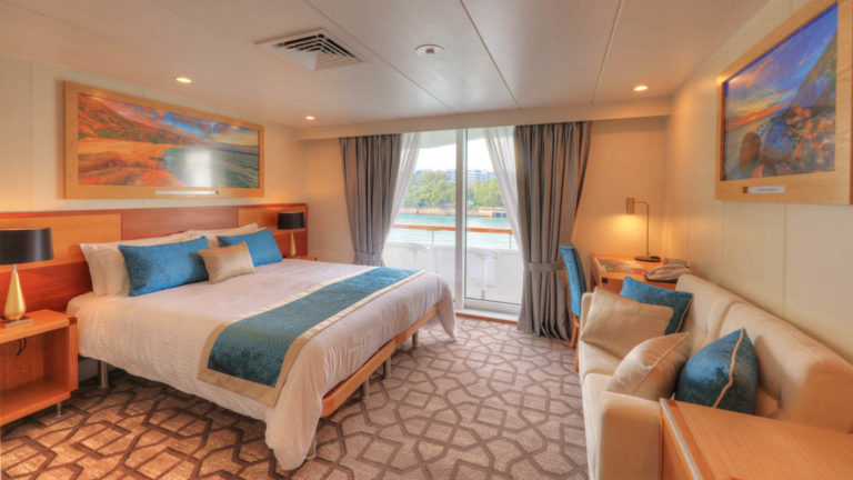 Bridge Deck Balcony stateroom aboard Coral Discoverer with large bed, couch, and balcony.