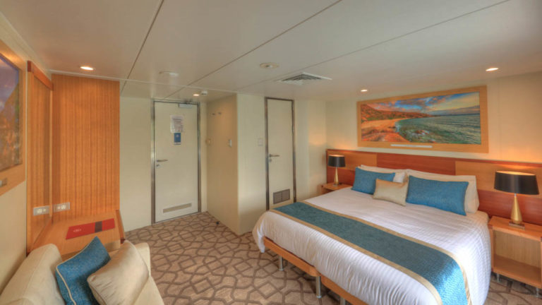 Bridge Deck Balcony stateroom aboard Coral Discoverer with large bed, couch, wardrobe, and doorway.