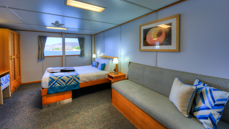Deluxe Stateroom aboard Coral Expeditions I with bed, couch, wardrobe, and window.
