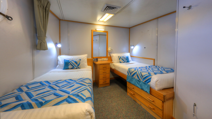 Cabin aboard Coral Expeditions I with two twin beds, mirror, and porthole.
