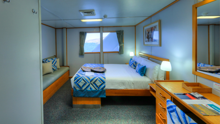 Stateroom aboard Coral Expeditions I with desk, couch, bed, and window.