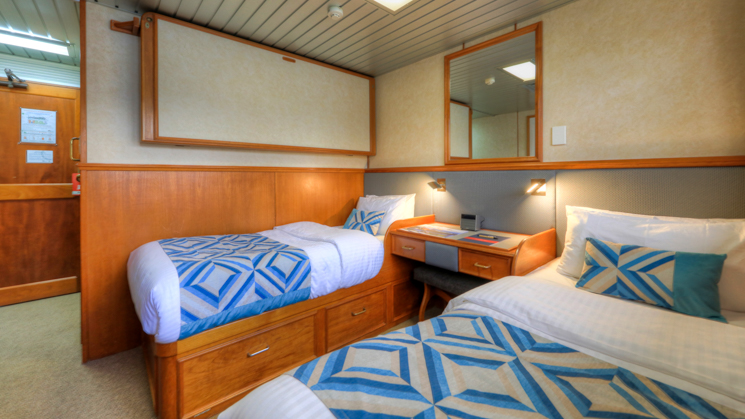 Two twin beds with bedside table and large mirror in cabin aboard Coral Expeditions II in Australia