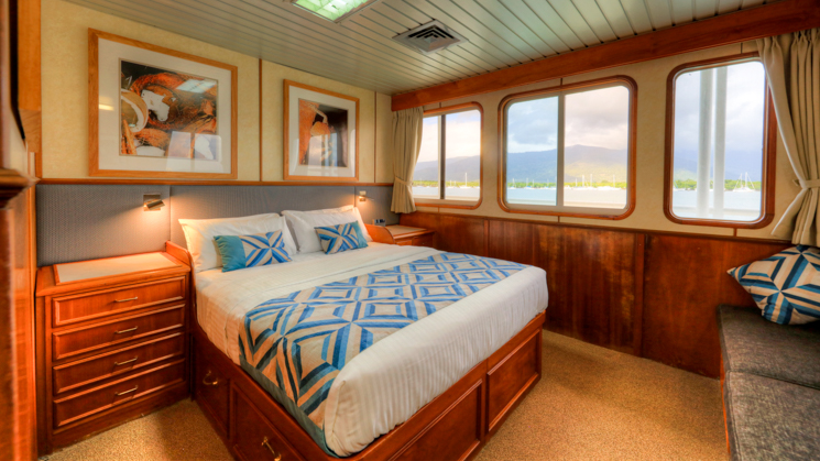 Deluxe Stateroom with bed, bedside tables, couch and three windows aboard Coral Expeditions II in Australia