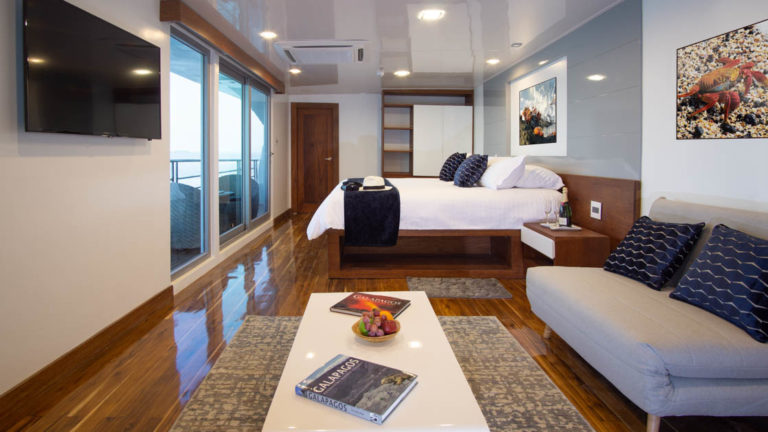 Galapagos Infinity yacht suite with couch, coffee table, king size bed floor to ceiling windows and balcony.