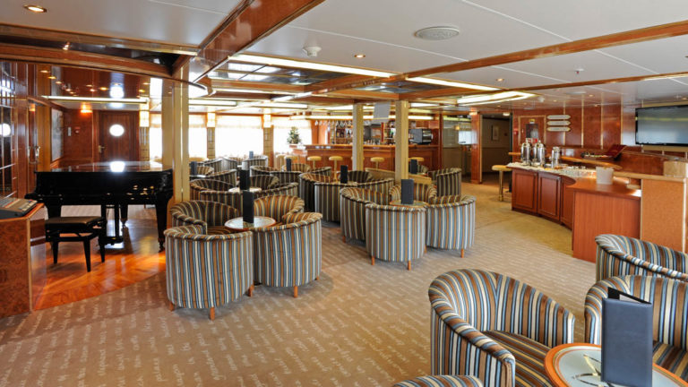 Lounge area with piano, chairs, cocktail tables, bar and service station aboard the Island Sky.