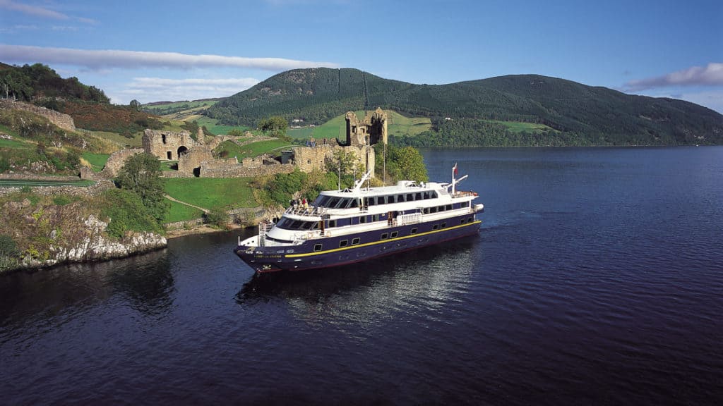 Small ship Lord of the Glens cruising past the Urquhart Castle in the Loch Ness highlands of Scotland
