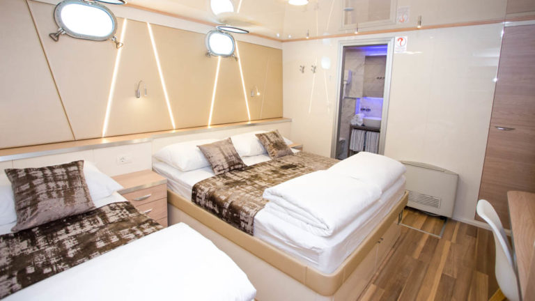Maritimo lower deck stateroom with 2 double beds, 2 portholes, bathroom, desk and chair.