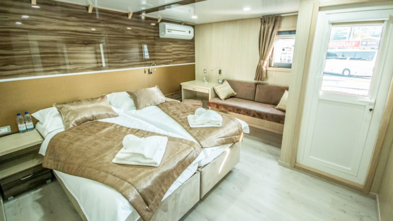 Markan VIP Upper Deck cabin with seating area, large double bed, door out to private balcony, nightstand and reading lights with large window.