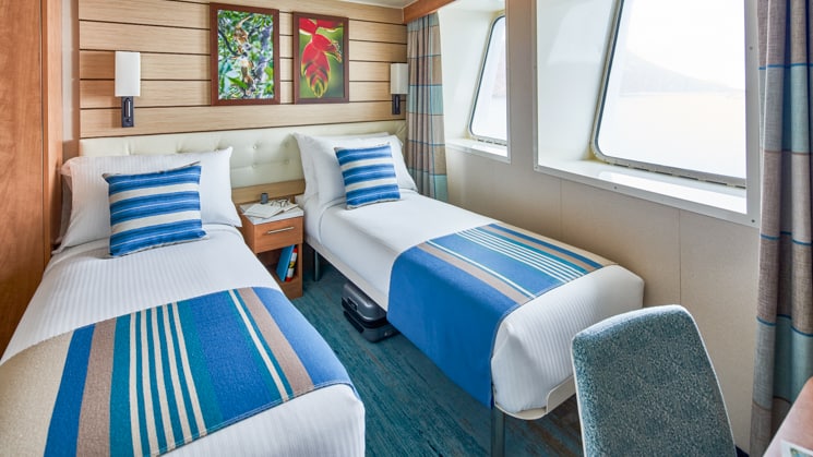 Two beds, nightstand, desk, chair and two windows in cabin aboard National Geographic Venture expedition ship