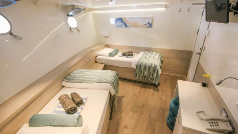 Cabin #13 with two fixed twin beds, two portholes, desk, phone, TV on wall and accents of white, wood and aqua aboard Nautilus Croatia & Mediterranean deluxe small yacht.