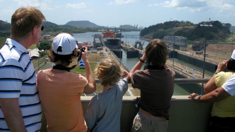 a family stands above the miraflores locks in panama on a sunny day pointing and taking pictures
