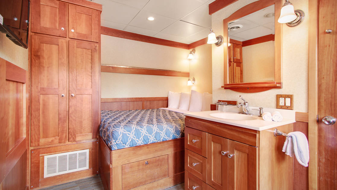 master stateroom with a large bed, nightstand and dresser aboard the Safari Explorer Hawaii small ship