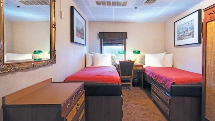 Two beds, nightstands, chair, dresser, window aboard Wilderness Legacy expedition ship