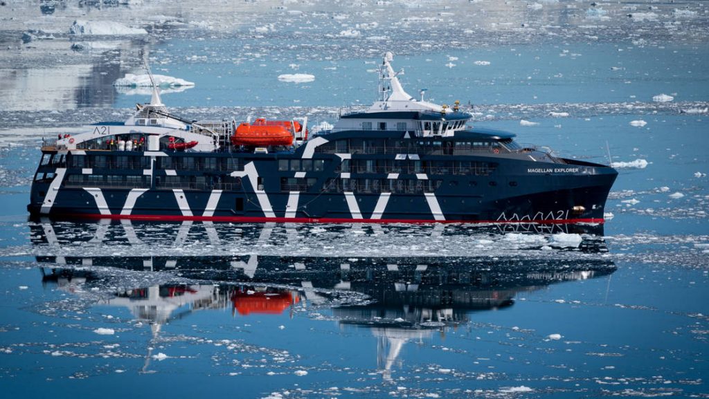 Exterior starboard side of dark navy blue Magellan Explorer Antarctica expedition ship floating on icy reflective ocean line