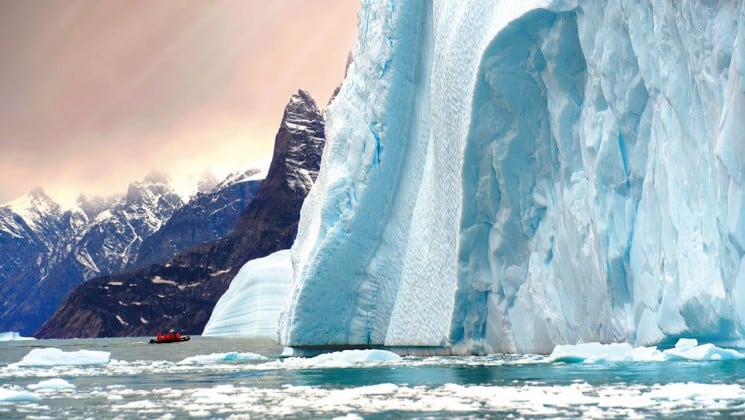 zodiac beside huge glacier as sun sets on arctic wildlife safari small ship cruise