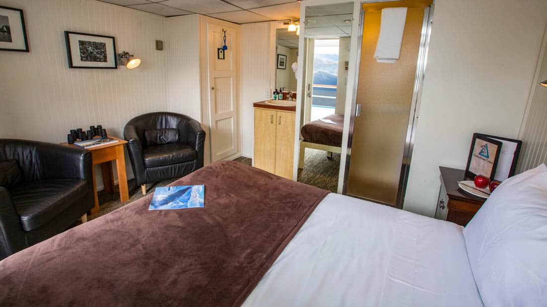 Category AAA stateroom aboard Baranof Dream with bed, sink, two chairs, and entry way.