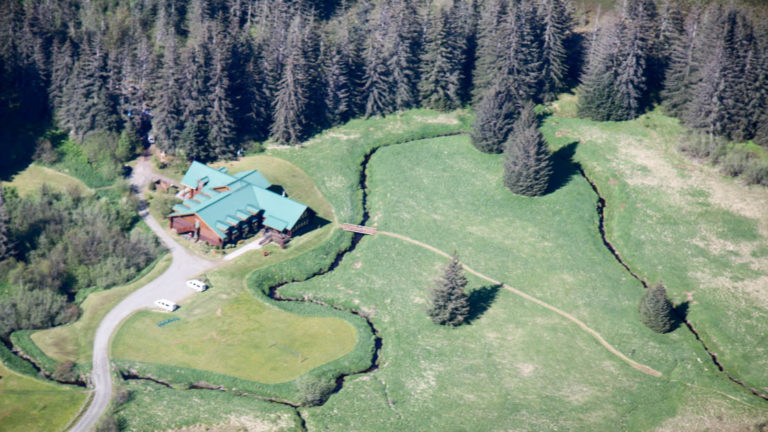 An aerial view of the Bear Track Inn, surrounded by large growth forests and open meadows in Alaska