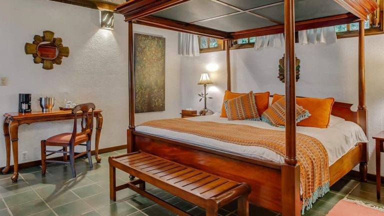 King sized canopy bed with wood detailing and small writing desk in garden suite bedroom at Chaa Creek Lodge in Belize.