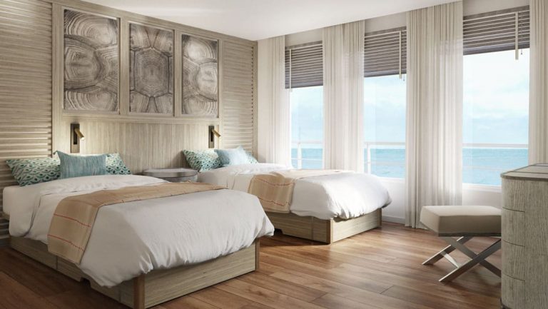 Suite on Conservation Galapagos ship with 2 twin beds in white linens, beige accents, desk & floor-to-ceiling windows.